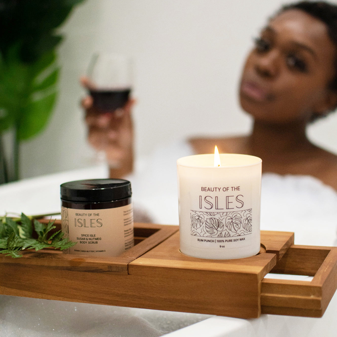 Relaxing bath scene with Beauty of the Isles soy candle and body scrub on a wooden tray, enhancing a soothing, spa-like experience.