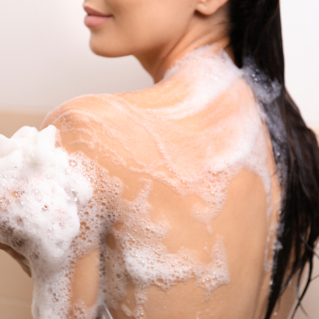 Woman using vegan marshmallow body wash, lathering foam, highlighting gentle cleansing and soothing ritual for sensitive skin.
