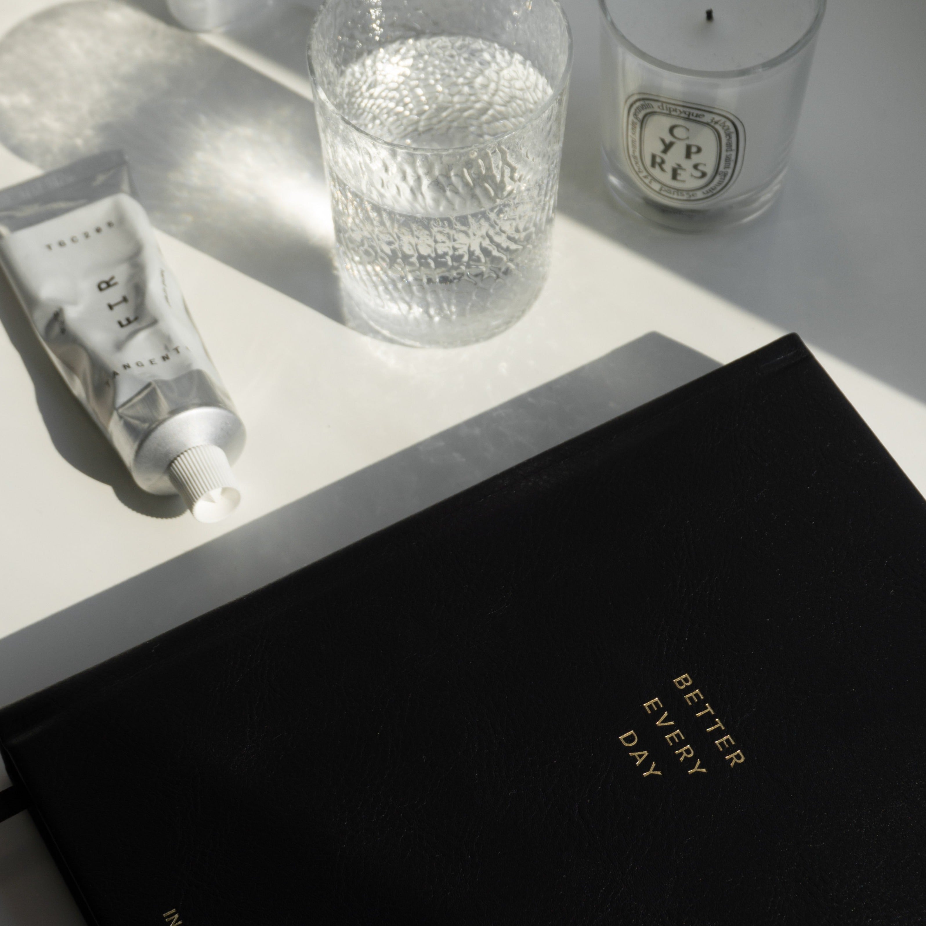 Flat lay of Better Every Day Journal with candle, tube, and glass on a white surface.