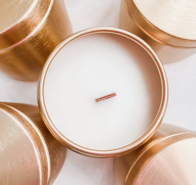 Top view of Citrus Basil & Agave beeswax candle with wood wick, surrounded by elegant gold containers.