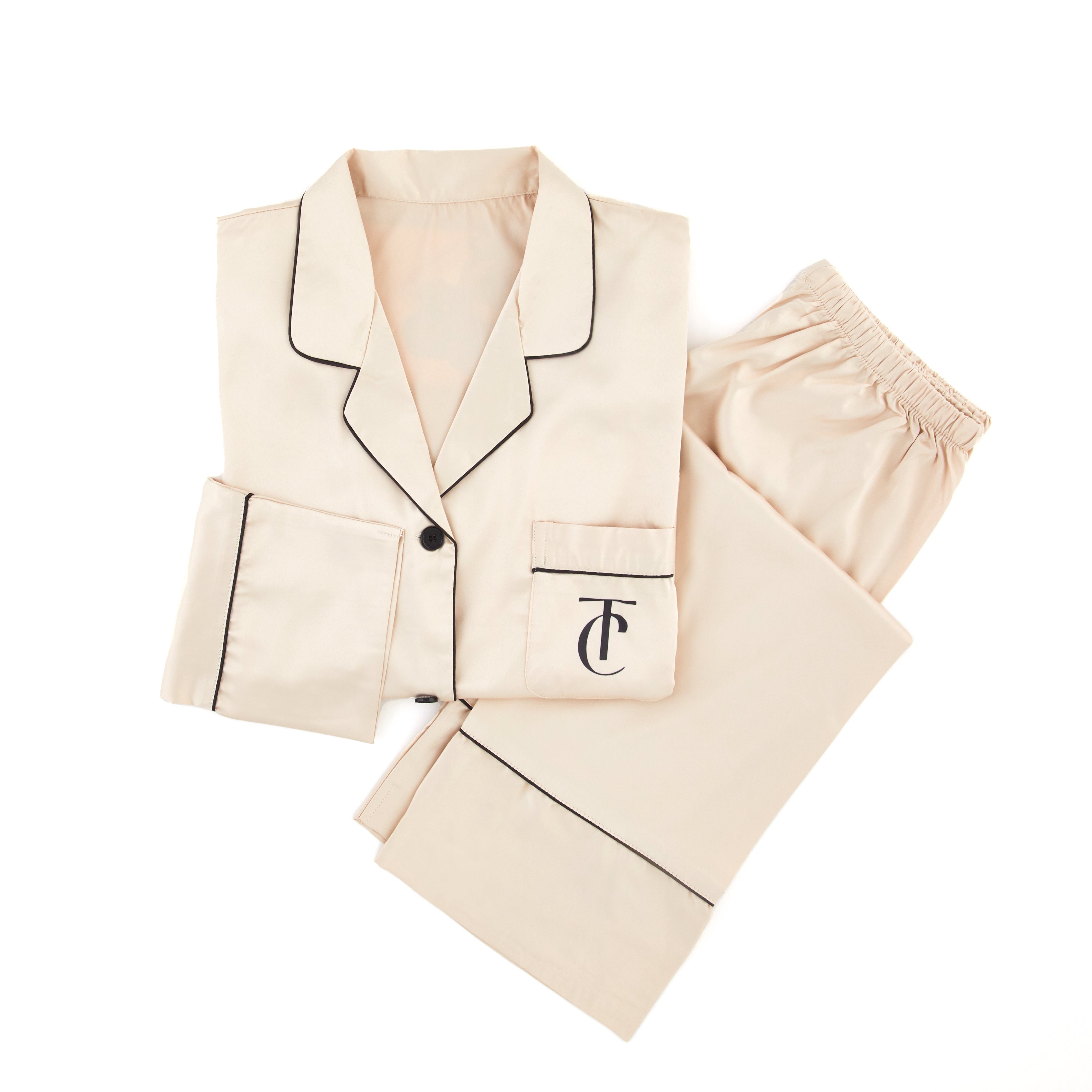 Alt Tag: Tsuri Signature Satin Pajamas in Bone/Black design, folded to show elegant black trim and embroidered logo, handcrafted luxury wear.