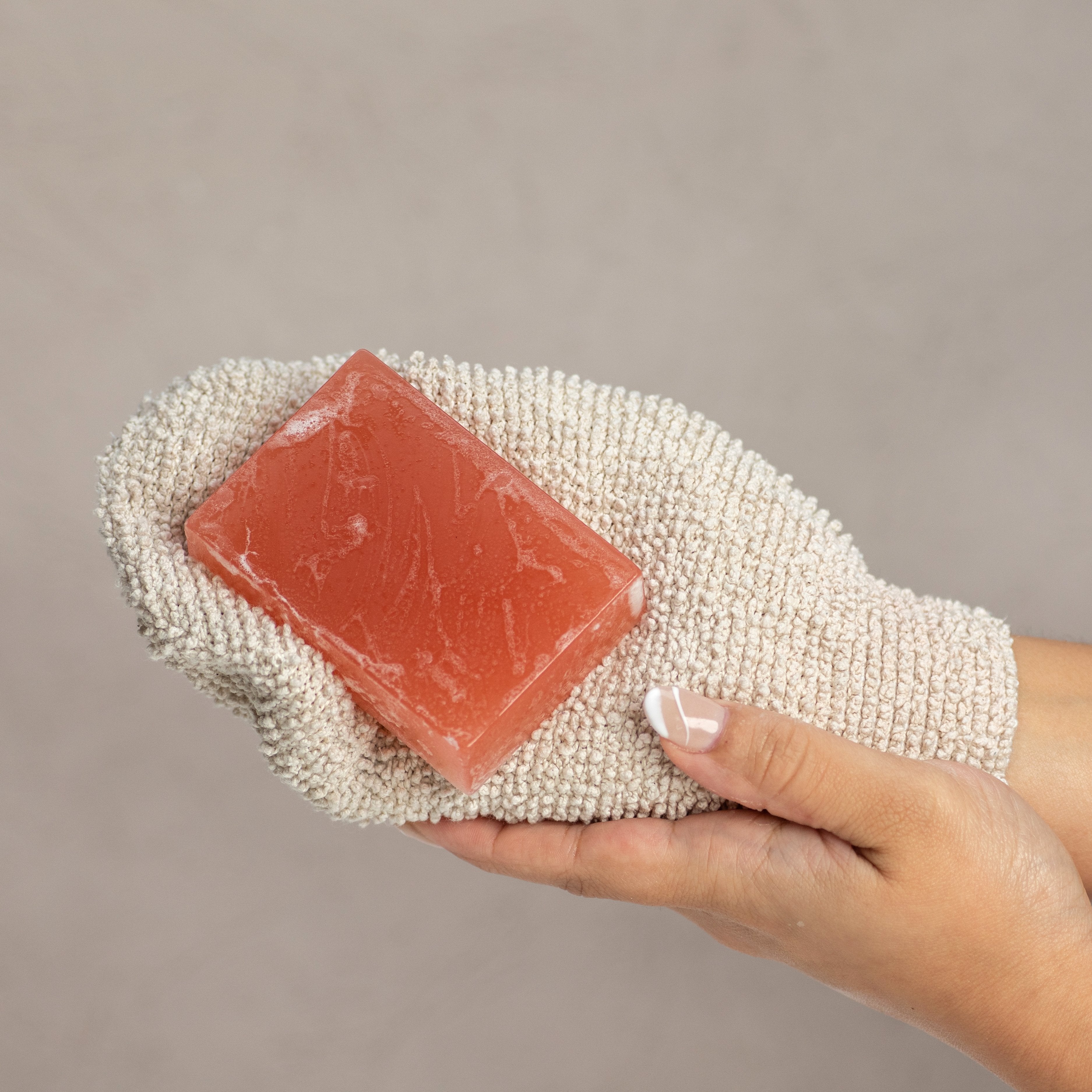 Hand holding a cashmere and vanilla glycerin bar soap on an exfoliating mitt