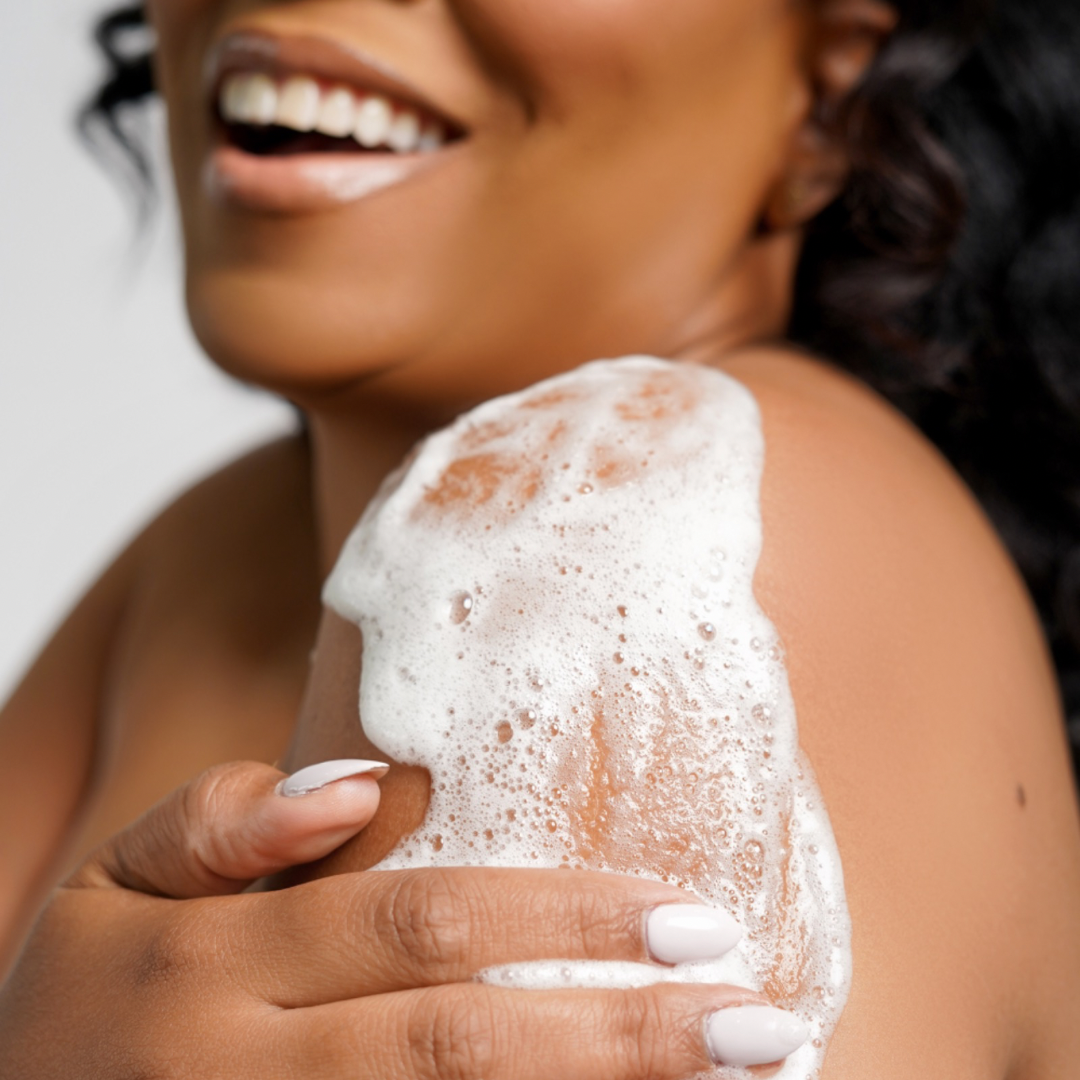 Joyful woman using Vegan Marshmallow Body Wash with rich foam on shoulder, showcasing smooth, hydrated skin.