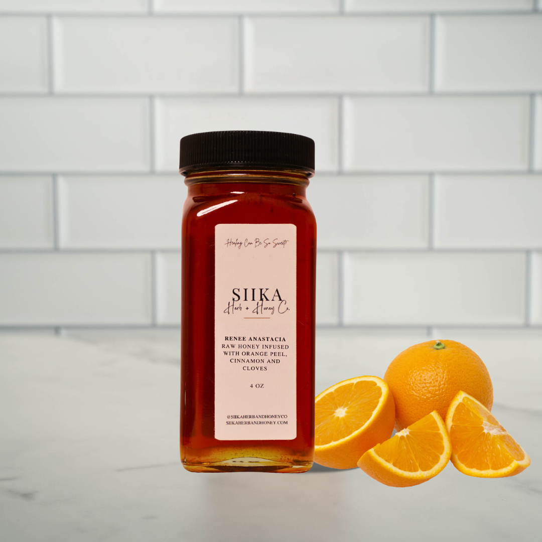 Renee Anastasia Orange Spice Honey with ginger, clove, and cinnamon, next to fresh oranges in a kitchen setting.