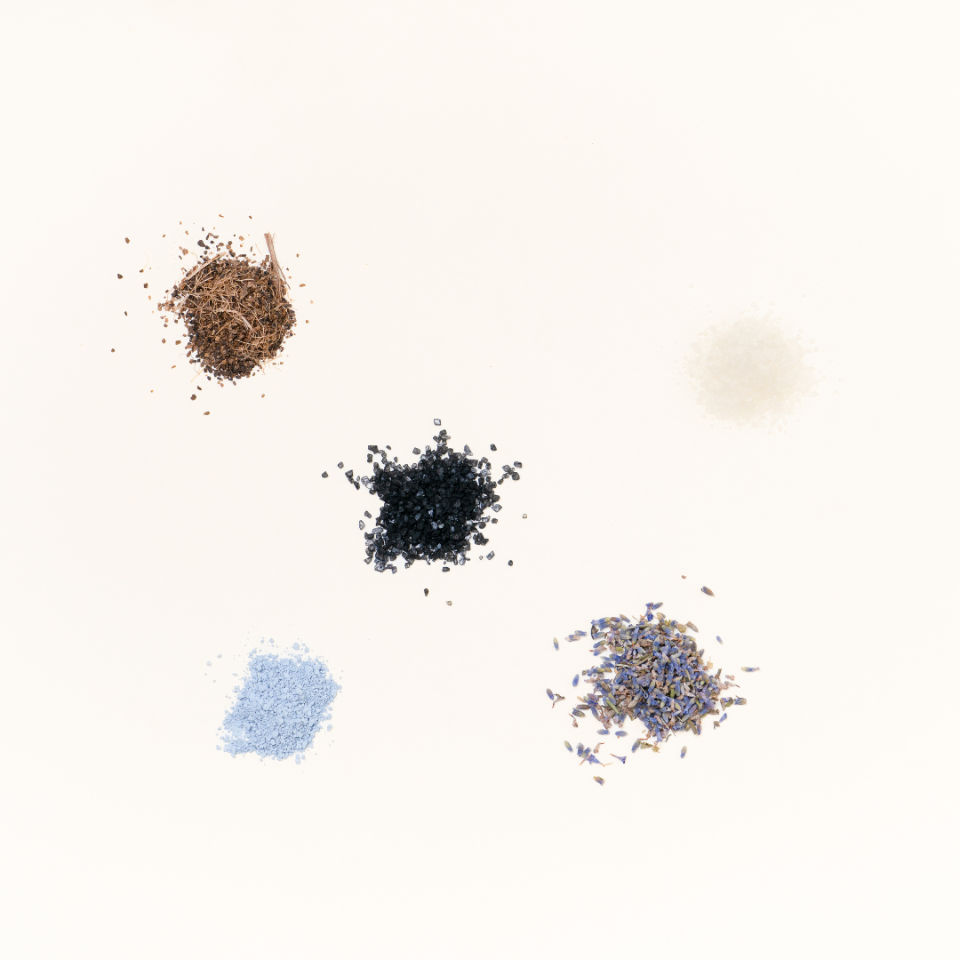 Natural ingredients for Gullah Bath Tea, featuring volcanic ash, lavender, oats, Himalayan salt, and herbs on a light background.