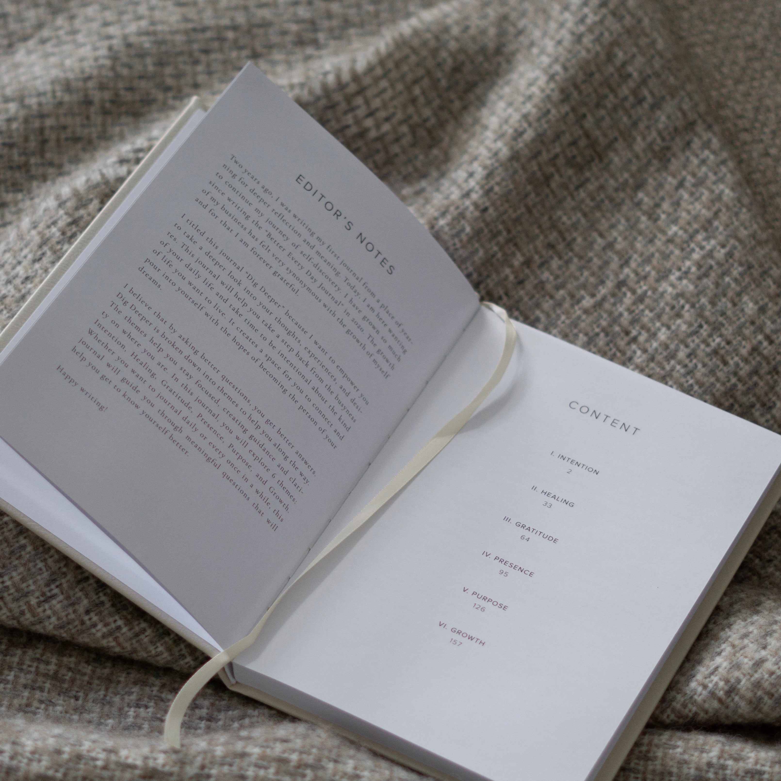 Open Dig Deeper Journal on cozy blanket, showing contents and editor's notes for healing, intention, and self-discovery.