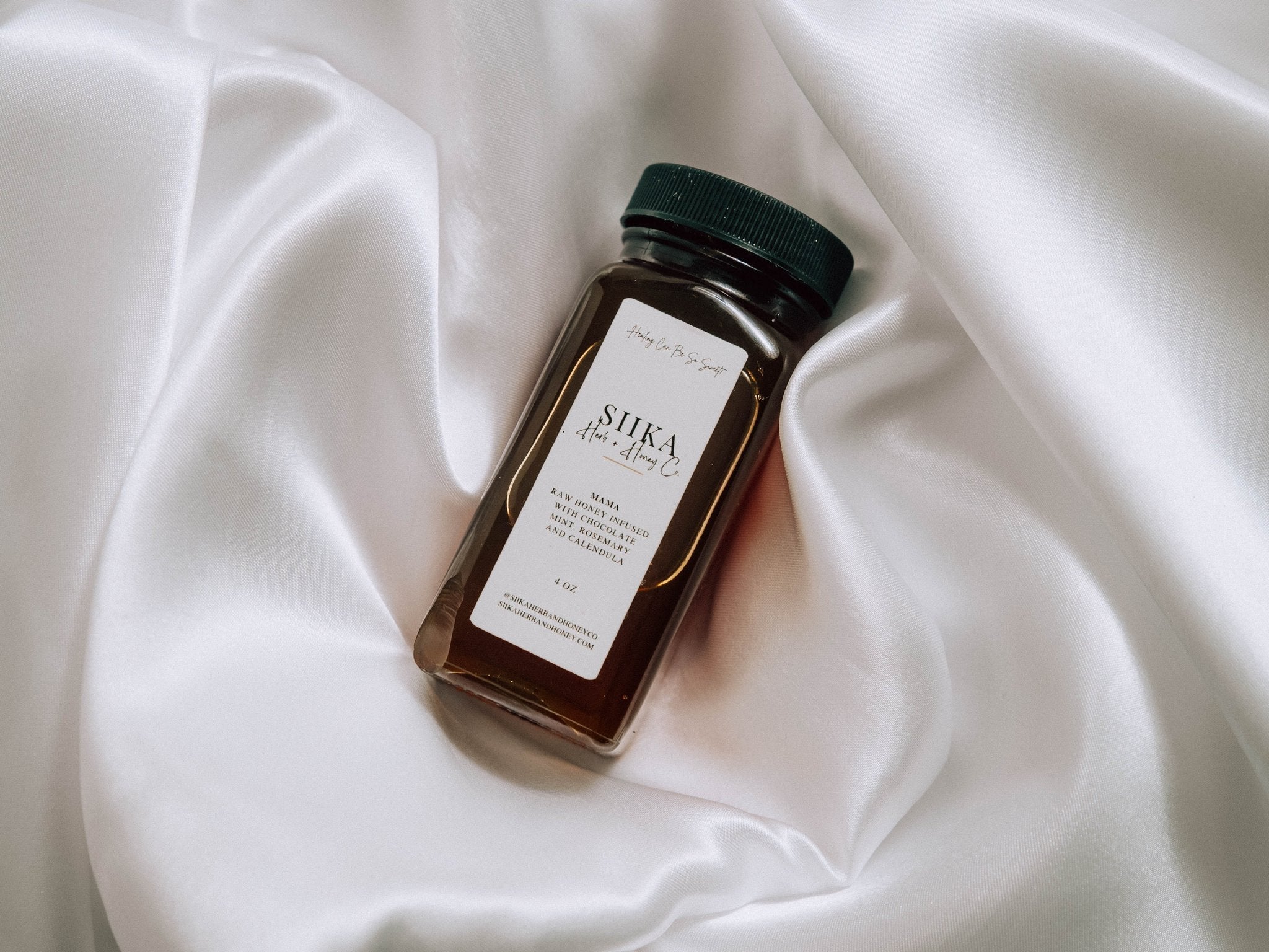 Jar of Mama Mint Rosemary Honey on satin, a versatile treat for desserts or skincare, enhancing taste and promoting skin healing.