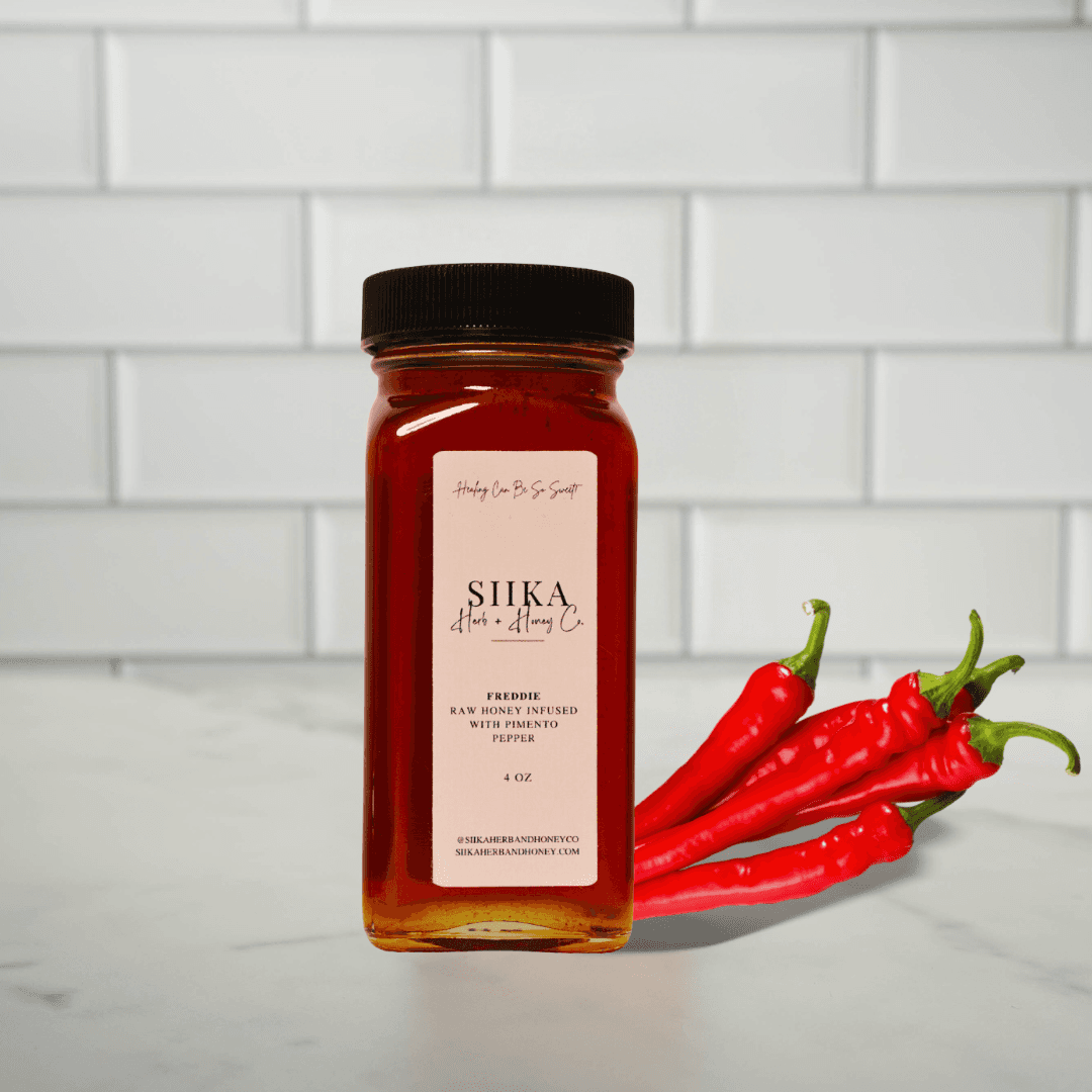 Freddie Sweet Chili Honey with pimento pepper against white tile, perfect for marinades and drizzling over vegetables and meats.